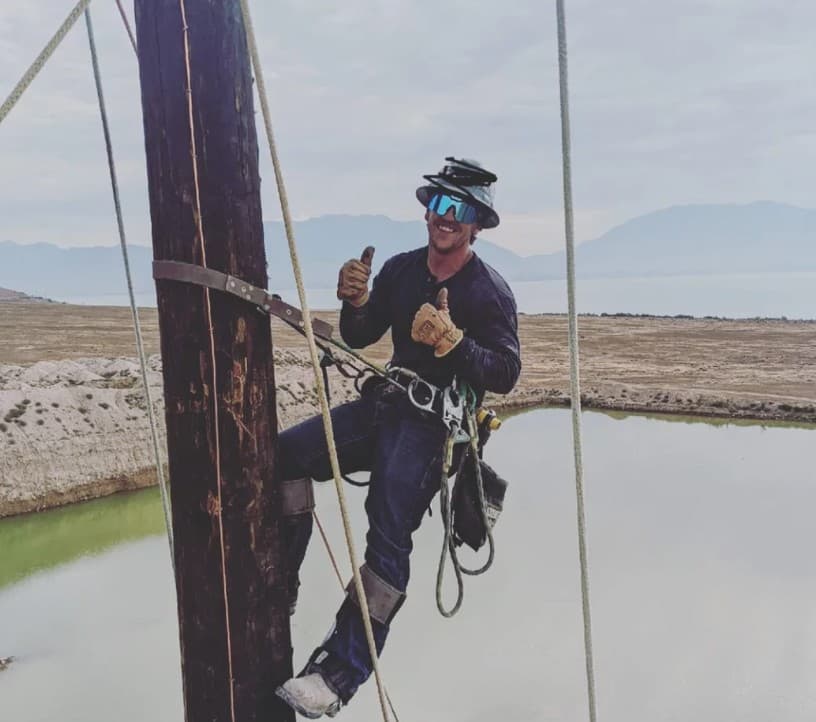 Lineworker climbing with a lake in the background