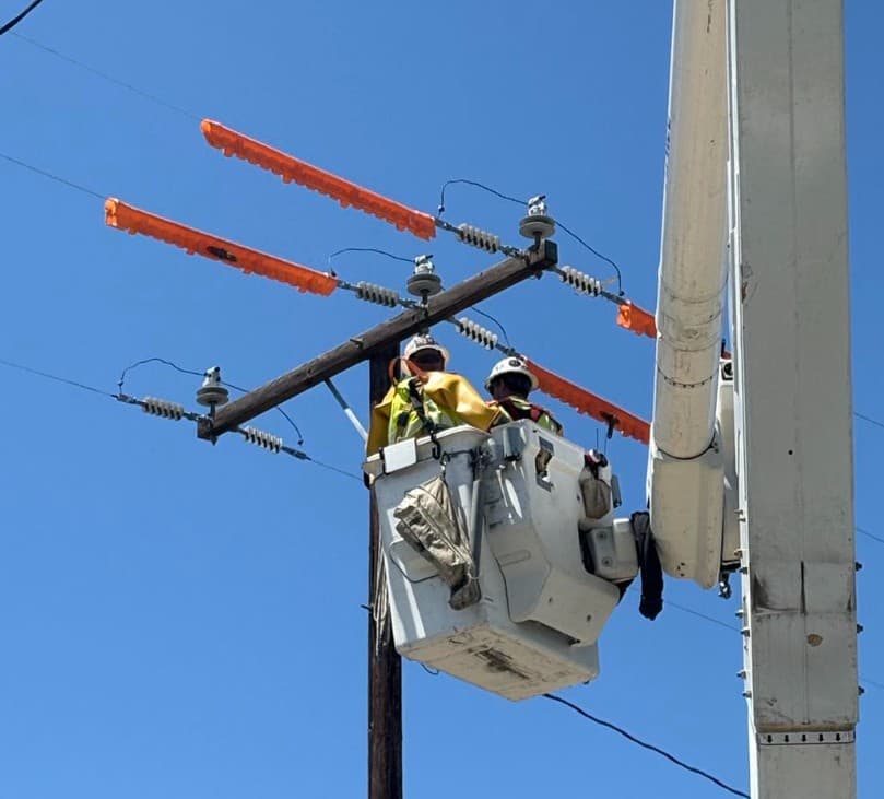 Two lineworkers in a bucket with orange line covers on energized conductors