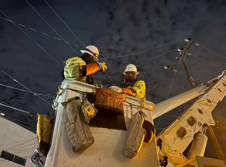 Two lineworkers in a bucket under night sky with orange rubber gloves