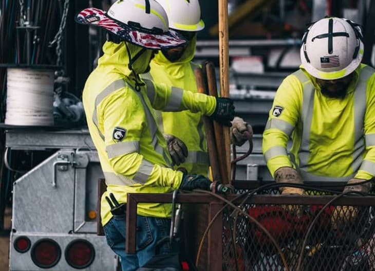 Three lineworkers in FR hoodies handling material at the truck