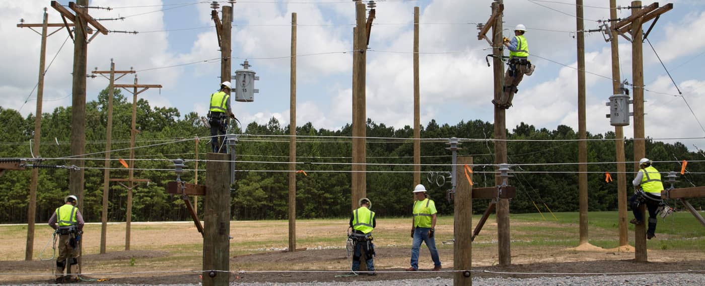 Students climbing poles at a lineman training yard